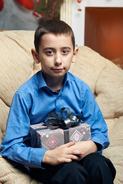 Happy boy in a comfortable chair near the tree by the fireplace received a gift.