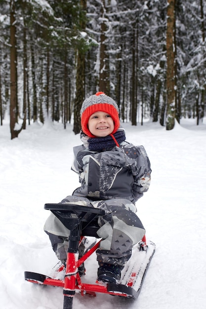 Happy boy downhill on a sled in winter a child in bright clothes sits on a sled snow is flying at him