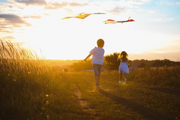 Happy boy and girl playing with kites in field at sunset Happy childhood concept