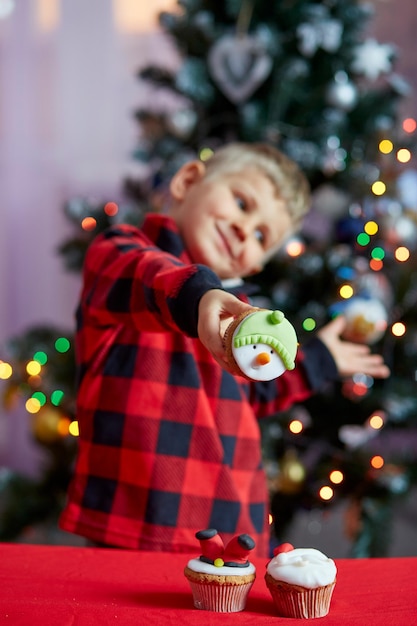 Happy boy holding creative cupcakes in front of Christmas tree Cozy Christmas time Good holidays mood Selective focus