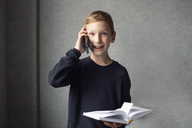 A happy boy is holding a book in his hands and talking on the phone