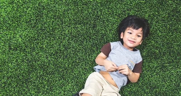 Happy boy is lying on artifact grass field top view