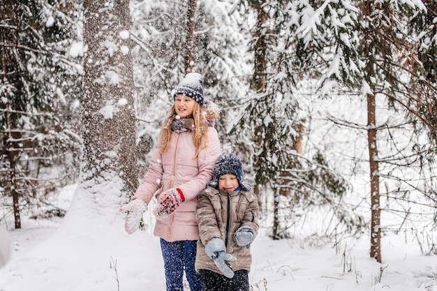 A happy boy is sitting in the snow next to a girl in the forest