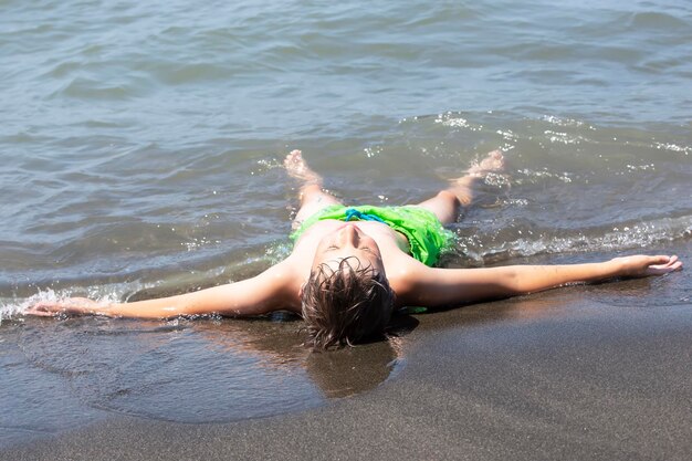 A happy boy lies in the sea, enjoys the waves and summer holidays. Child on vacation at the seaside.