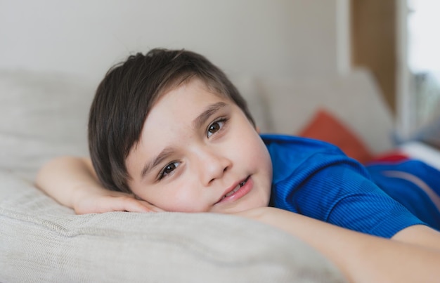 Happy boy lying on sofa looking up at camera with smiling faceClose up face a Child resting in living room with light shining from window on sunny day spring or summerKid relaxing at home on weekend