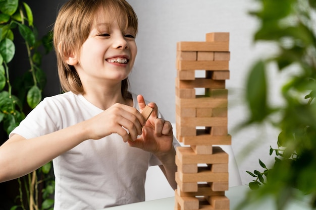 Happy boy playing board game building a tower of wooden cubes jenga logic game for child development