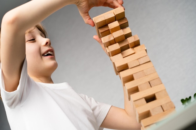 Happy boy playing board game building a tower of wooden cubes jenga logic game for child development