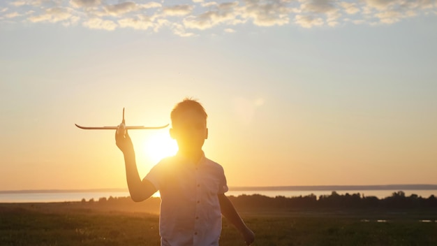 Happy boy runs on meadow playing with toy airplane at sunset