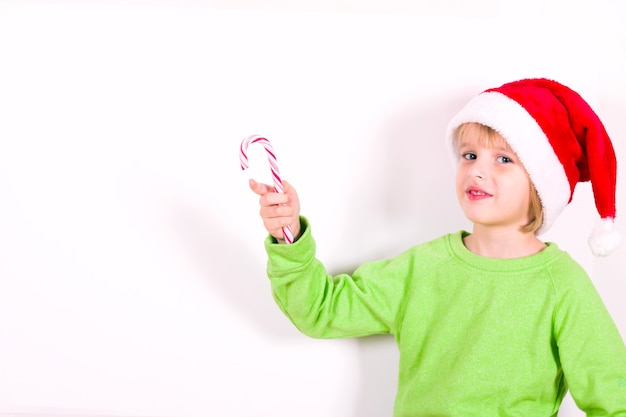 Happy boy in Santa red hat holding candy in hand. Christmas concept.