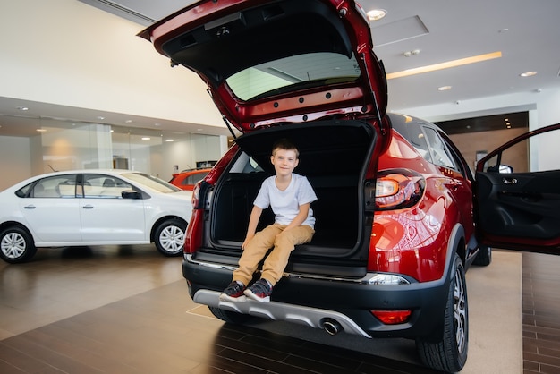 Happy boy sitting in the trunk of a new car at a dealership