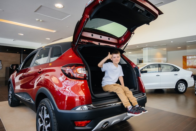 Happy boy sitting in the trunk of a new car at a dealership