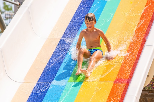 A happy boy on water slide in a swimming pool having fun during summer vacation in a beautiful aqua park. A boy slithering down the water slide and making splashes.