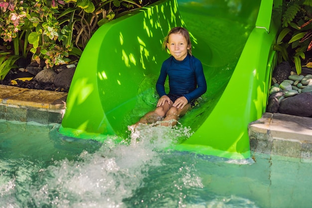 Happy boy on water slide in a swimming pool having fun during summer vacation in a beautiful tropical resort