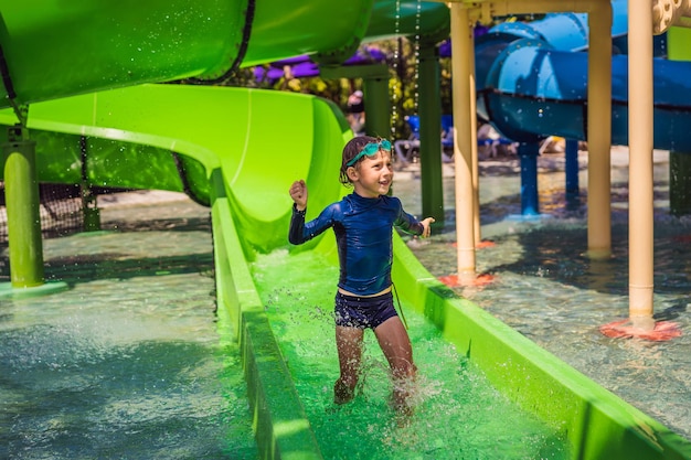 Happy boy on water slide in a swimming pool having fun during summer vacation in a beautiful