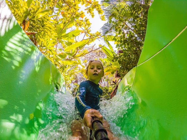 Happy boy on water slide in a swimming pool having fun during summer vacation in a beautiful