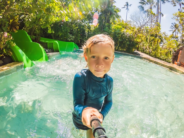 Happy boy on water slide in a swimming pool having fun during summer vacation in a beautiful