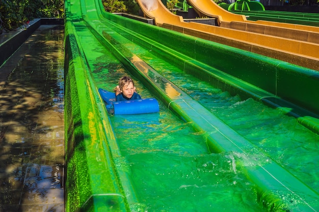 Happy boy on water slide in a swimming pool having fun during summer vacation in a beautiful