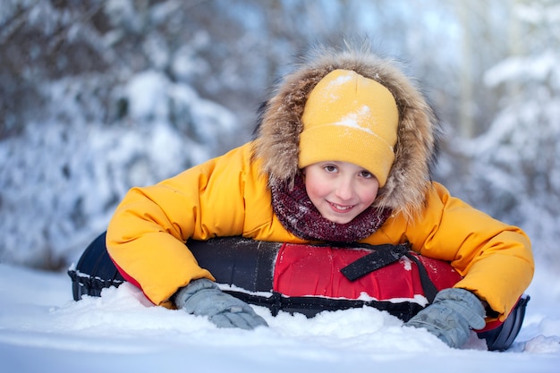 Happy boy in winterwear smiling riding a tubing in winter park. Child sledding. Boy kid play outdoors in snow.