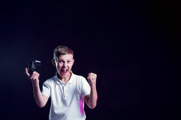 Happy boy with open mouth and joystick shouting for joy after winning in video game on black wall