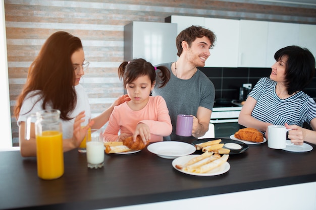 Happy breakfast of a large family in the kitchen. Siblings, parents and children, mother and grandmother. Father and daughter. Everyone is eating in the morning and chatting and having fun.