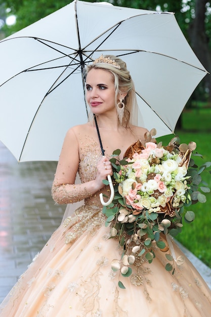 The happy bride with a white umbrella in the rain, in the summer in the park. Open-air wedding.