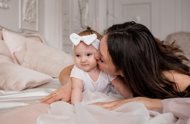 Happy brunette mom is lying on the bed with her baby daughter and kissing Single mother