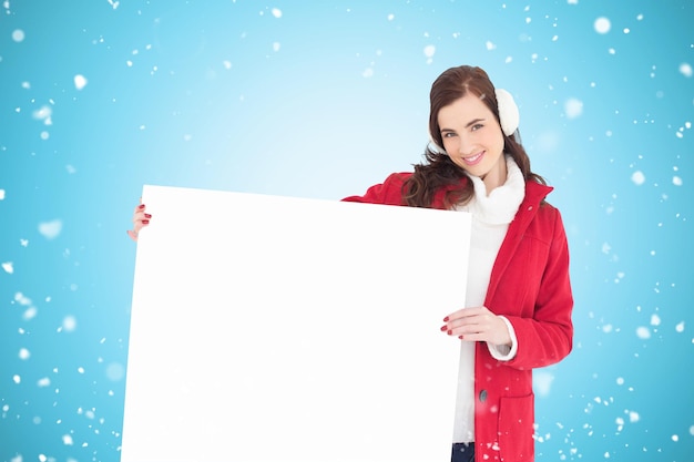 Happy brunette showing white poster against blue vignette