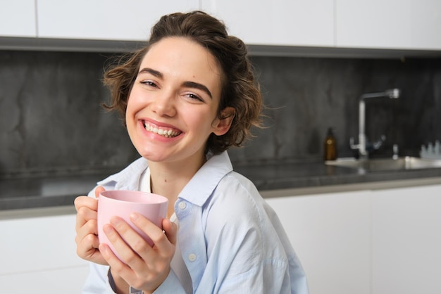 Happy brunette woman drinking coffee at home girl with pink cup sits in her kitchen and enjoys