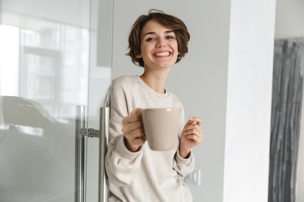 Happy brunette woman drinking coffee at home