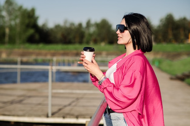 Happy brunette woman in sunglasses walking near the lake on wooden pier in sunny day