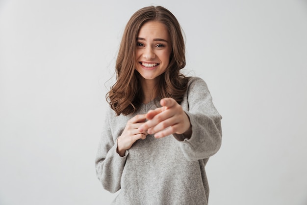 Happy brunette woman in sweater pointing  over grey wall