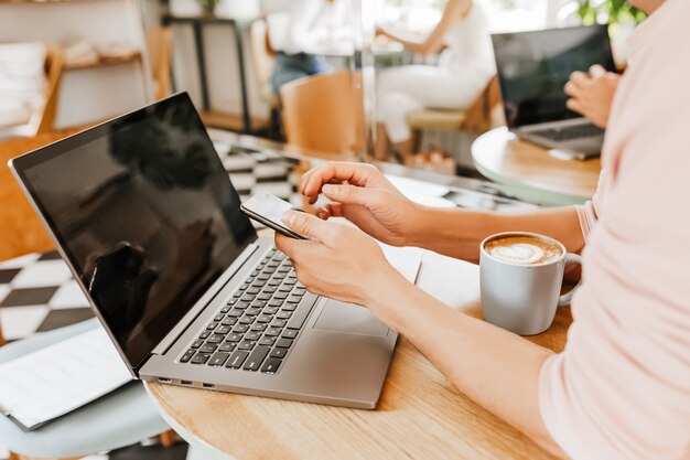 Happy business man sitting at cafeteria with laptop and smartphone. Businessman texting on smart phone while sitting in a cafe, working and checking email on computer