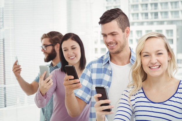 Happy business people using smartphones while standing in row 