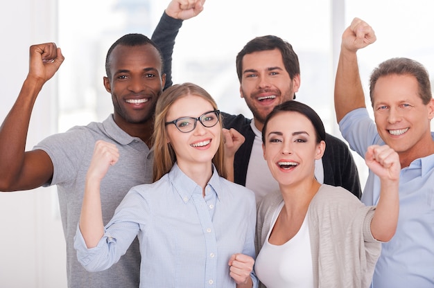 Happy business team. Group of cheerful business people in casual wear standing close to each other and keeping arms raised