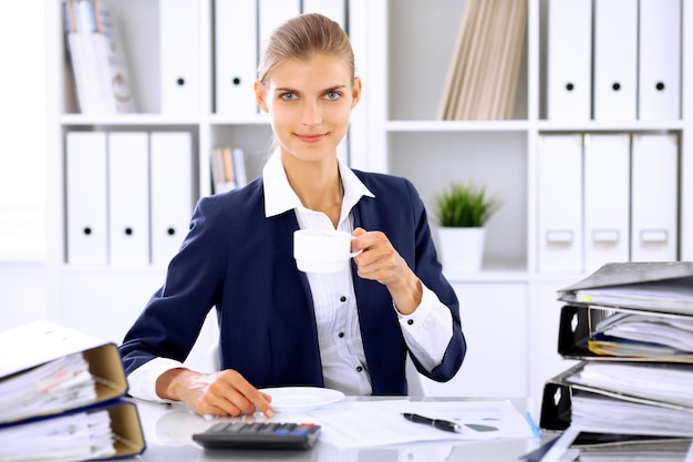 Happy business woman or female accountant having some minutes for coffee and pleasure at working place