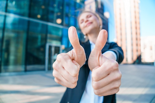 Happy business woman showing thumbs up while standing outdoors against office