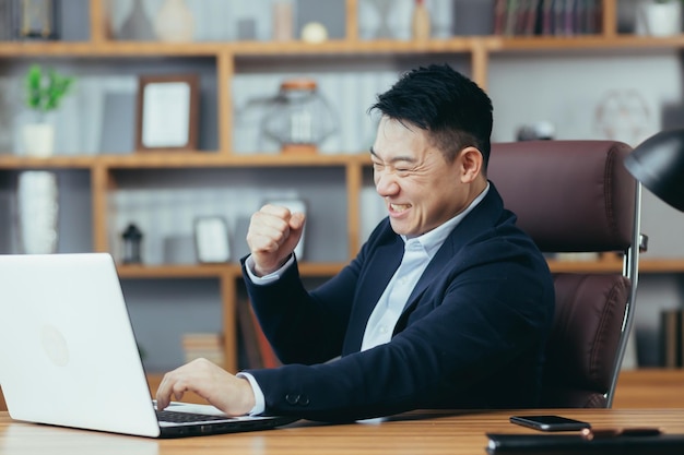 Happy businessman celebrates the conclusion of a successful contract looks at the laptop screen and rejoices