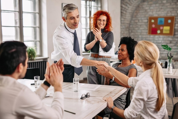 Happy businessman congratulating his colleague on job well done and handshaking during business meeting in the office