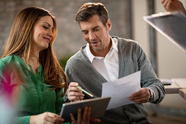 Happy businessman and his female colleague going through paperwork and using digital tablet in the office