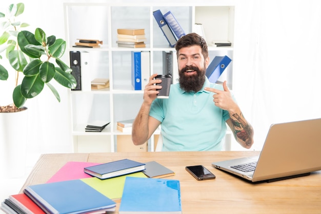 Happy businessman pointing finger at coffee cup sitting at office desk takeaway