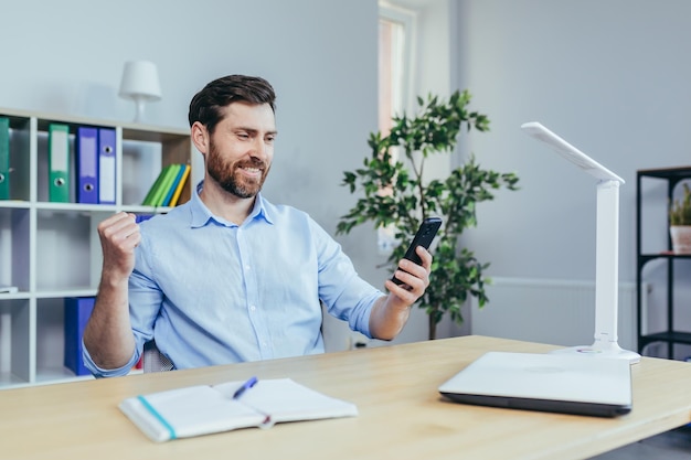 Happy businessman reading good news from the phone man working in the office