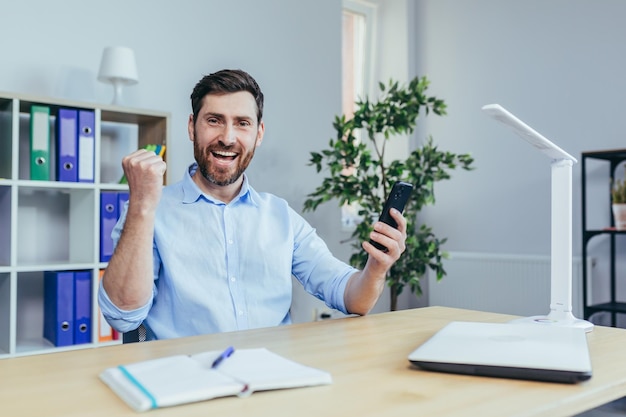 Happy businessman reading good news from the phone man working in the office