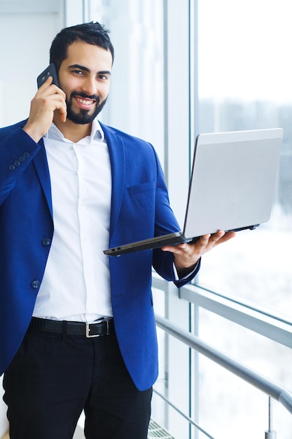 Happy businessman talking on mobile phone and holding in arms laptop