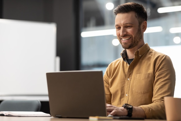 Happy businessman typing using laptop sitting at workplace in office