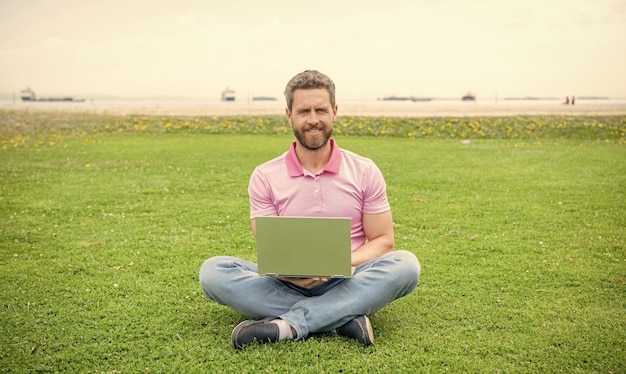 Happy businessman using laptop for blogging on green grass freelancer