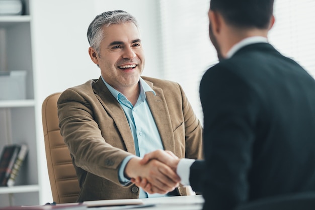 The happy businessmen handshaking near the desk