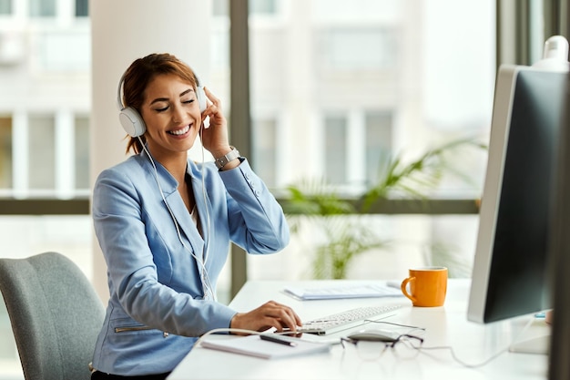 Happy businesswoman enjoying with eyes closed while listening music over headphones in the office