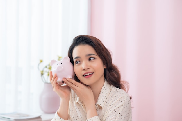 Happy businesswoman holding piggy bank against pink wall