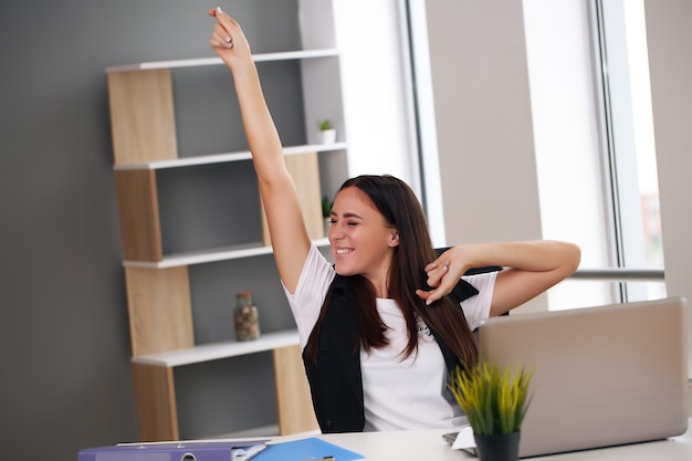 Happy businesswoman with raised so hand gesture reading letter on desk in front of laptop