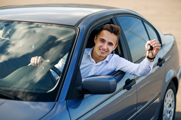 Happy buyer holding car keys inside his new vehicle